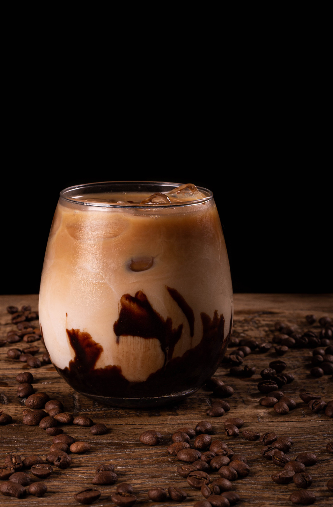 A delicious iced coffee with chocolate swirls in a glass, surrounded by coffee beans, highlighting the rich and indulgent flavors of Coffee Secrets' specialty coffee.