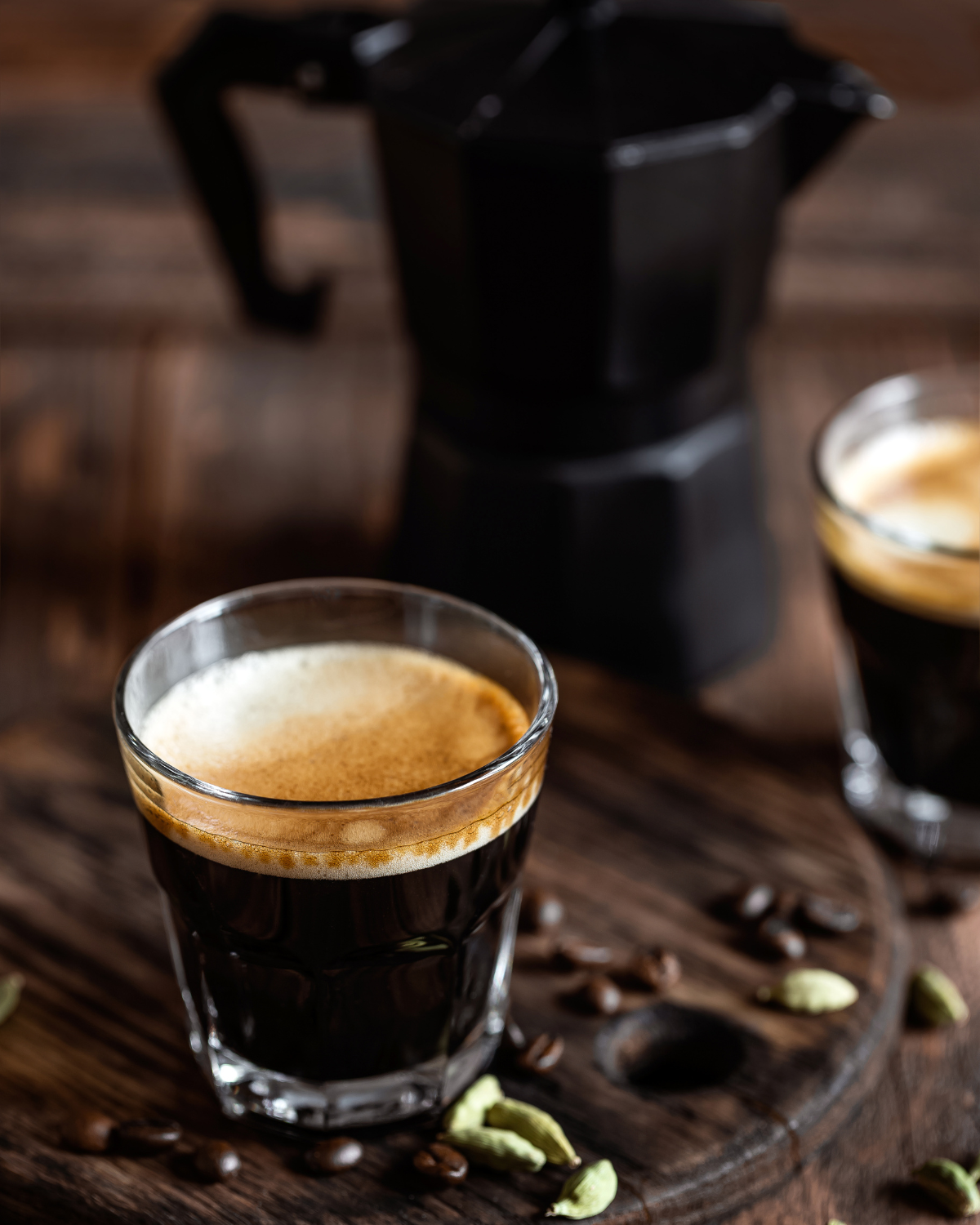 Freshly brewed espresso in a glass cup on a wooden table, with coffee beans and spices scattered around, showcasing the peak flavor of Coffee Secrets' same-day roasted coffee.