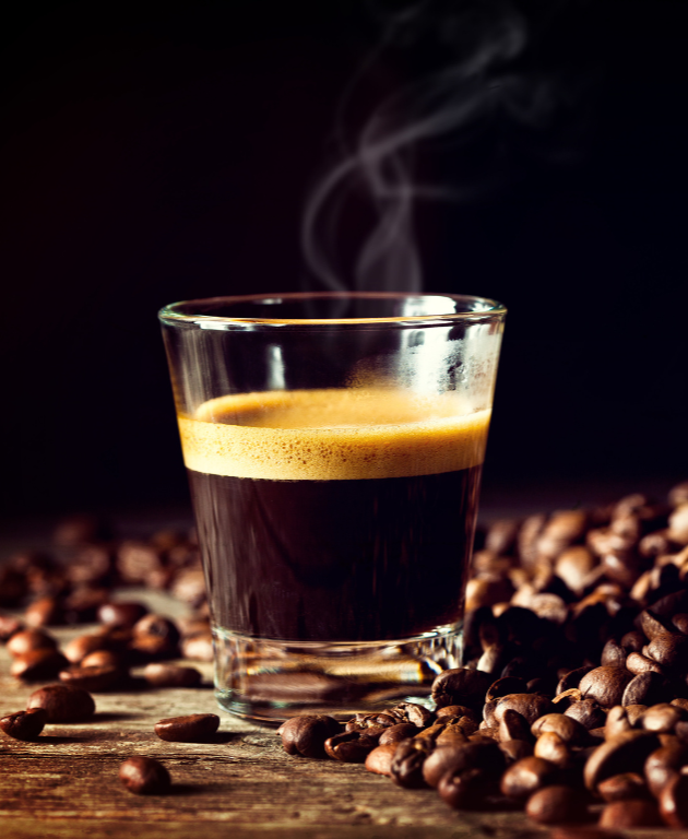 A steaming glass of freshly brewed espresso surrounded by coffee beans, highlighting the rich and inviting aroma of Coffee Secrets' specialty coffee.